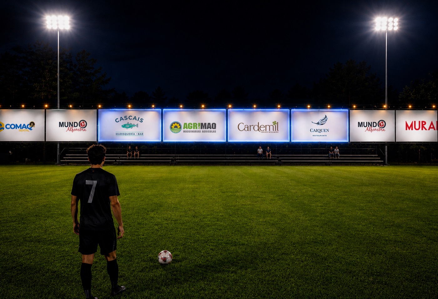 Módulos publicitarios iluminados en el perímetro de la cancha durante un partido nocturno